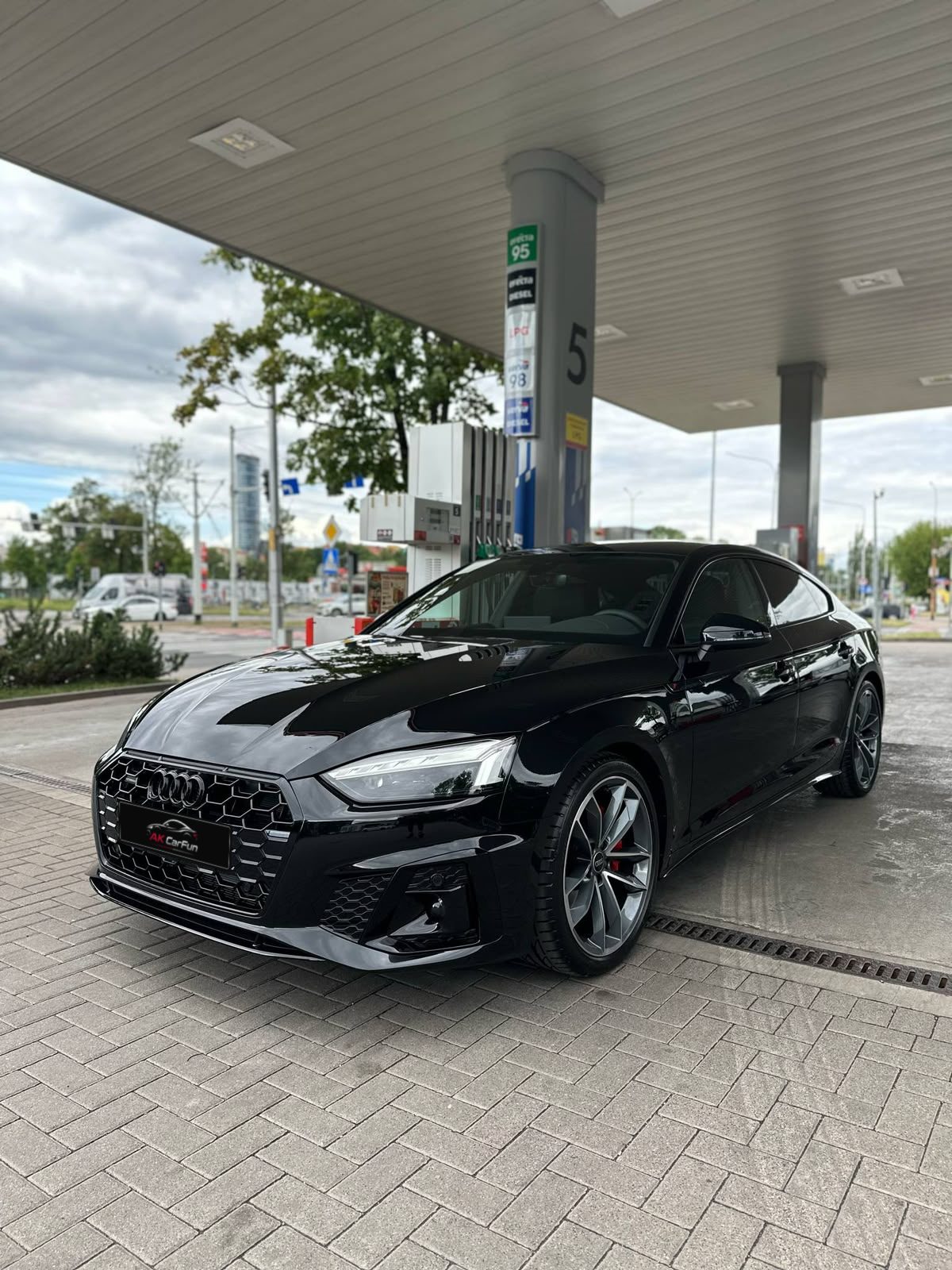 Czarne Audi A5 Sportback z przodu, pod wiatą stacji paliw, z tablicą AK CarFun