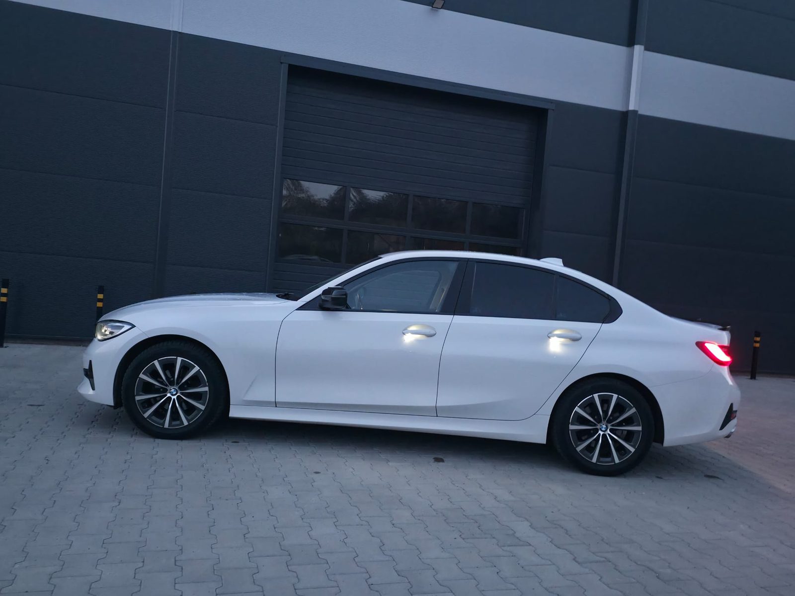 Białe BMW 318i G20 2020 z profilu, przed halą