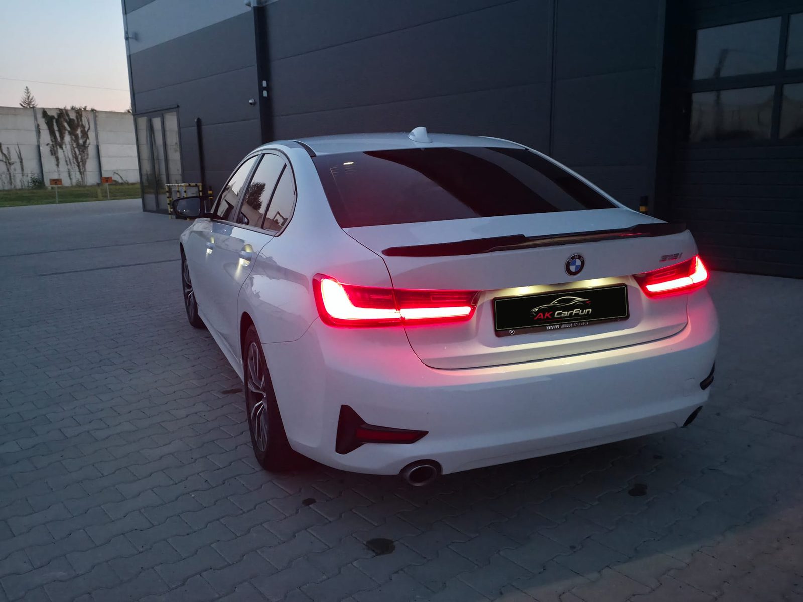 Tył białego BMW 318i G20 2020 z włączonymi światłami i tablicą AK CarFun