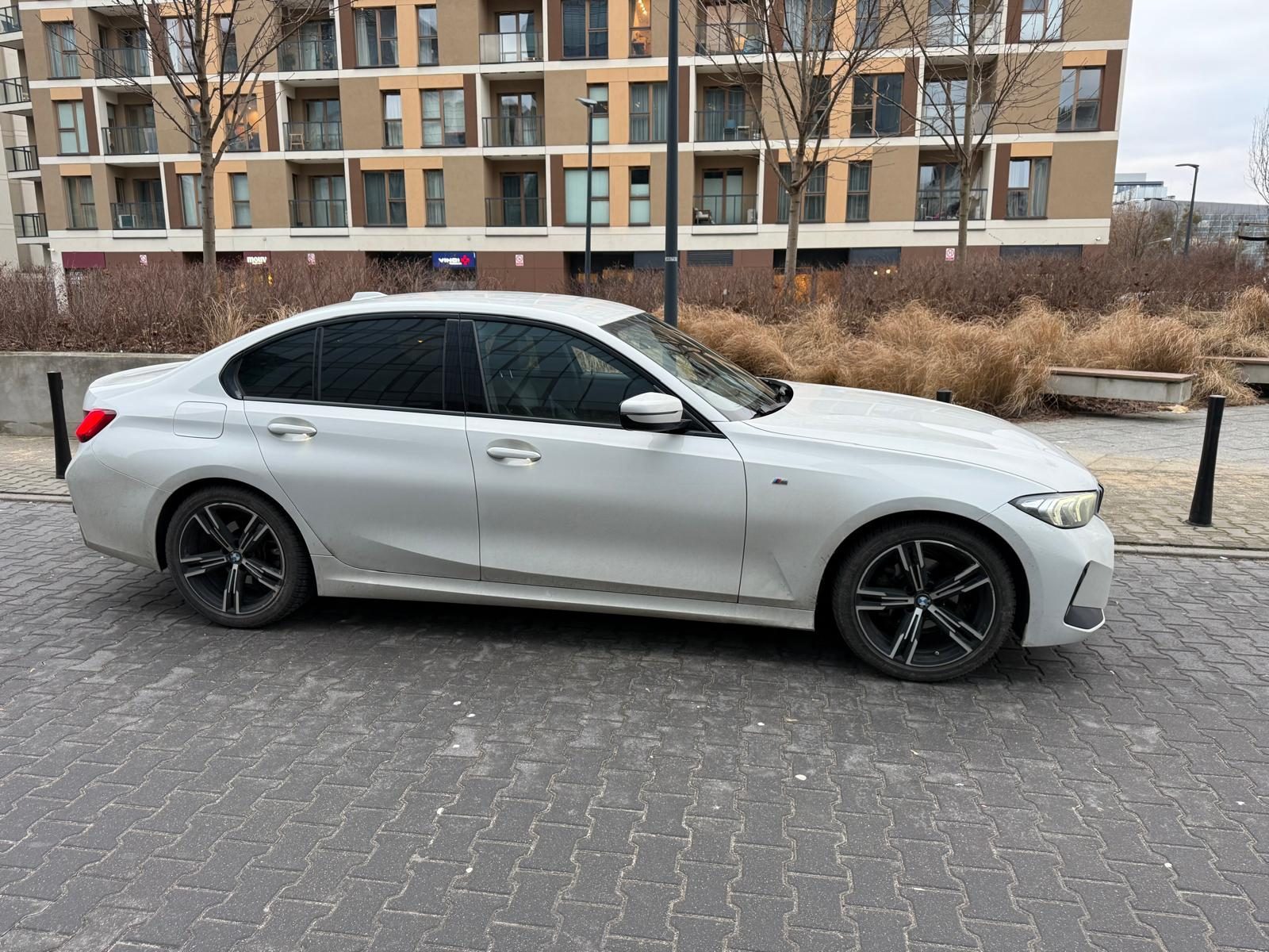 BMW 318i G20 2023 z boku, na placu przed nowoczesnymi budynkami