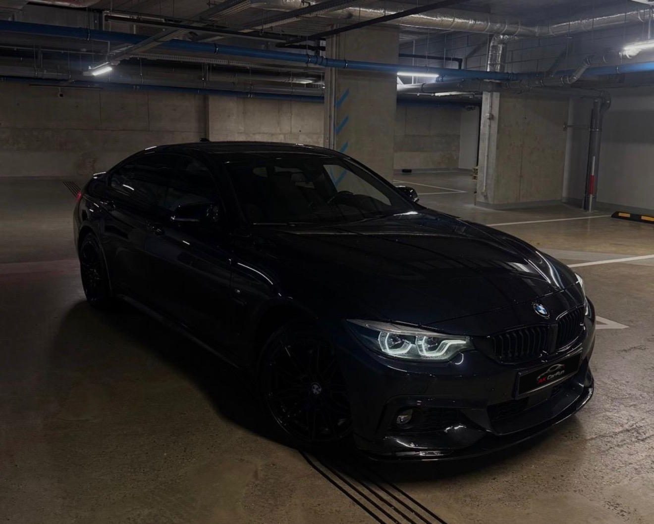 Czarne BMW nocą w podziemnym garażu, widok z przodu na reflektory i tablicę z logo AK CarFun